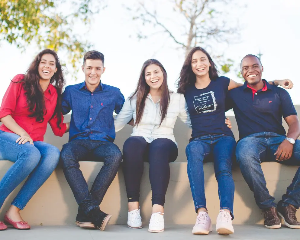 Five people sitting on a ledge outdoors, smiling with arms around each other, representing new patient registration form available at Natalie Yang Orthodontics in Vacaville, CA