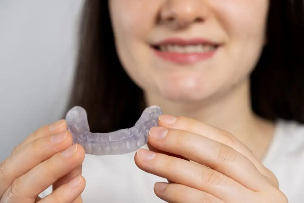 Smiling person holds a clear dental aligner, showing a mouth guard alternative at Natalie Yang Orthodontics Orthodontics in Vacaville, CA.