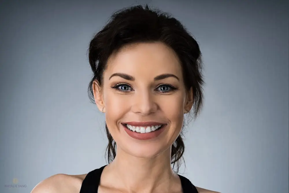 Smiling woman with dark hair against a gray background. She is wearing a black top as one of the Alternatives to Braces in Vacaville, CA.