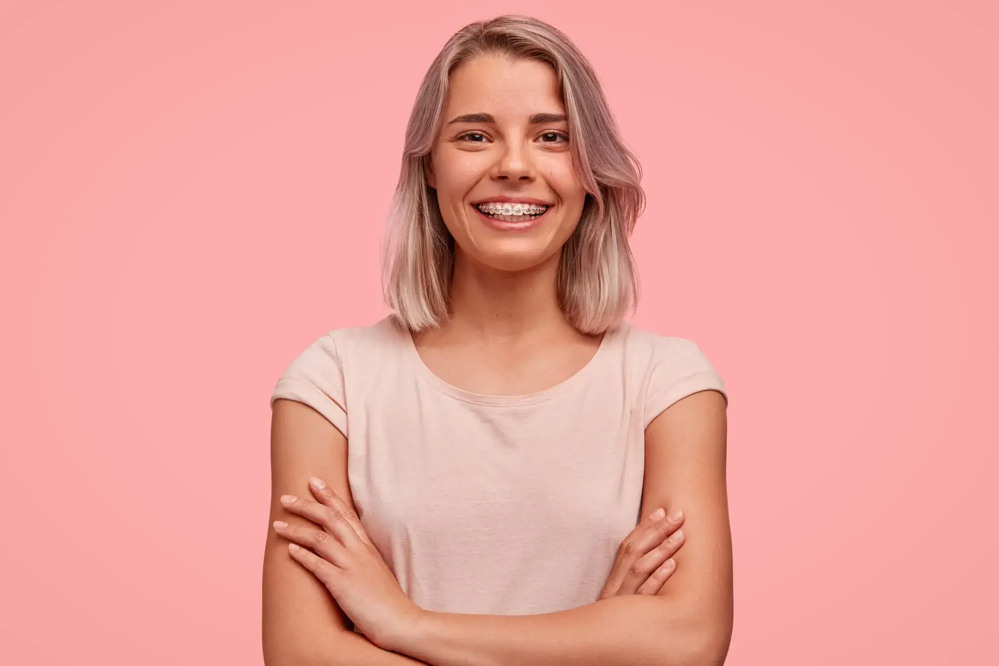 Young woman with shoulder-length blonde hair and metal braces smiles with arms crossed, standing in Vacaville, CA. Young woman with shoulder-length blonde hair and metal braces smiles with arms crossed, standing in Vacaville, CA.