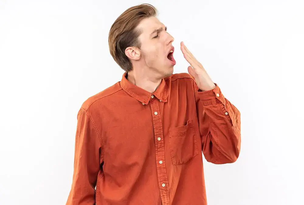A man in an orange shirt yawns and covers his mouth with his hand against a plain white background, representing the classic mouth breather look—an issue Natalie Yang Orthodontics Orthodontics can help address in Vacaville, CA. A man in an orange shirt yawns and covers his mouth with his hand against a plain white background, representing the classic mouth breather look—an issue Natalie Yang Orthodontics Orthodontics can help address in Vacaville, CA.
