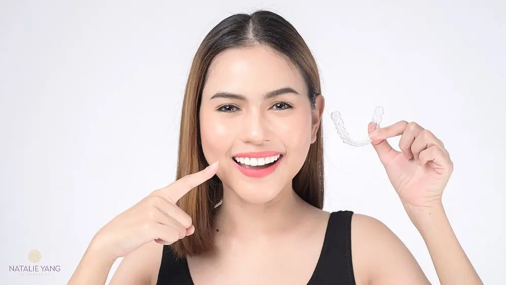 Smiling woman pointing at clear aligners, highlighting her Invisalign treatment with confidence after understanding about Does Insurance Cover Invisalign in Vacaville, CA.