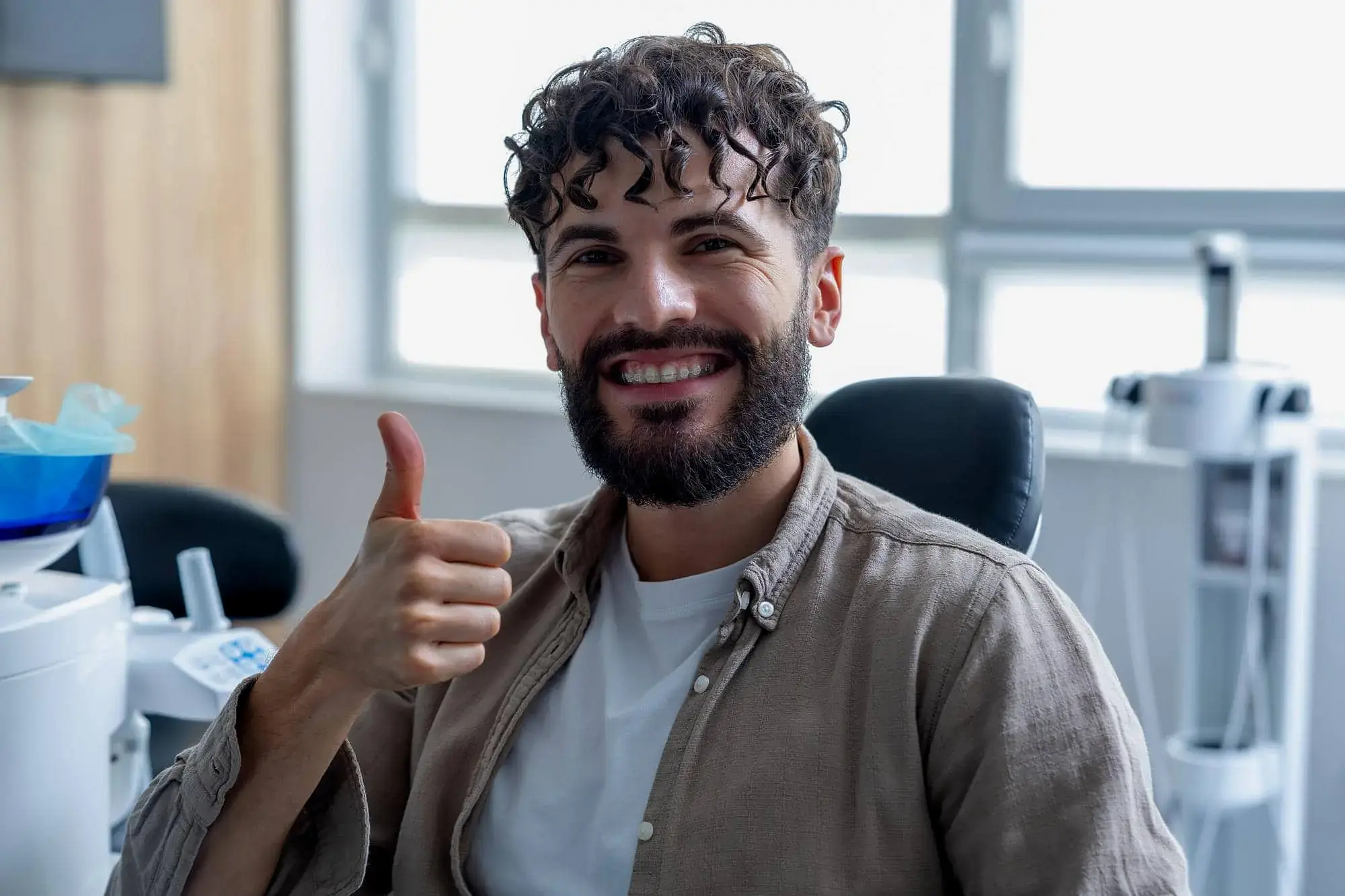 A smiling man shows Adult Braces ceramic braces at Natalie Yang Orthodontics in Vacaville, CA, giving a thumbs-up indoors. A smiling man shows Adult Braces ceramic braces at Natalie Yang Orthodontics in Vacaville, CA, giving a thumbs-up indoors.