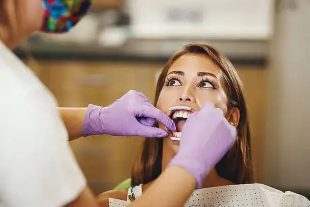 A dentist in Vacaville, CA at Natalie Yang Orthodontics checks a woman's Lingual Braces adult braces with purple gloves and tools. A dentist in Vacaville, CA at Natalie Yang Orthodontics checks a woman's Lingual Braces adult braces with purple gloves and tools.