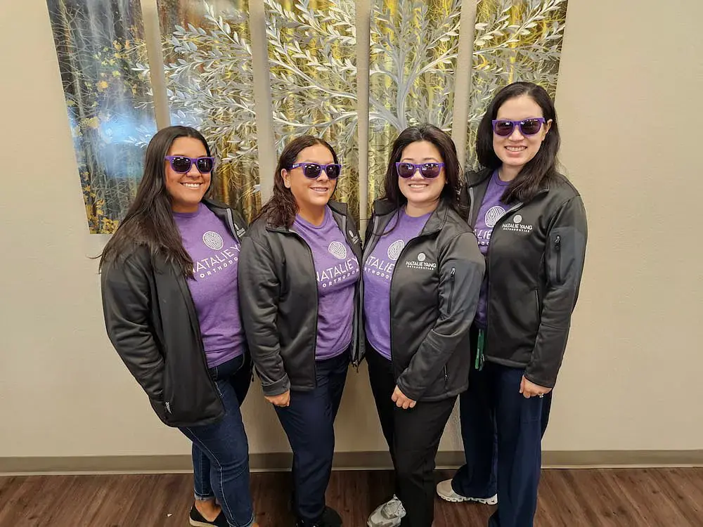 Smiling in front of metallic leaf art, four women in purple outfits show off orthodontic smiles and Orthodontic Appliances at Natalie Yang Orthodontics in Vacaville, CA. Smiling in front of metallic leaf art, four women in purple outfits show off orthodontic smiles and Orthodontic Appliances at Natalie Yang Orthodontics in Vacaville, CA.
