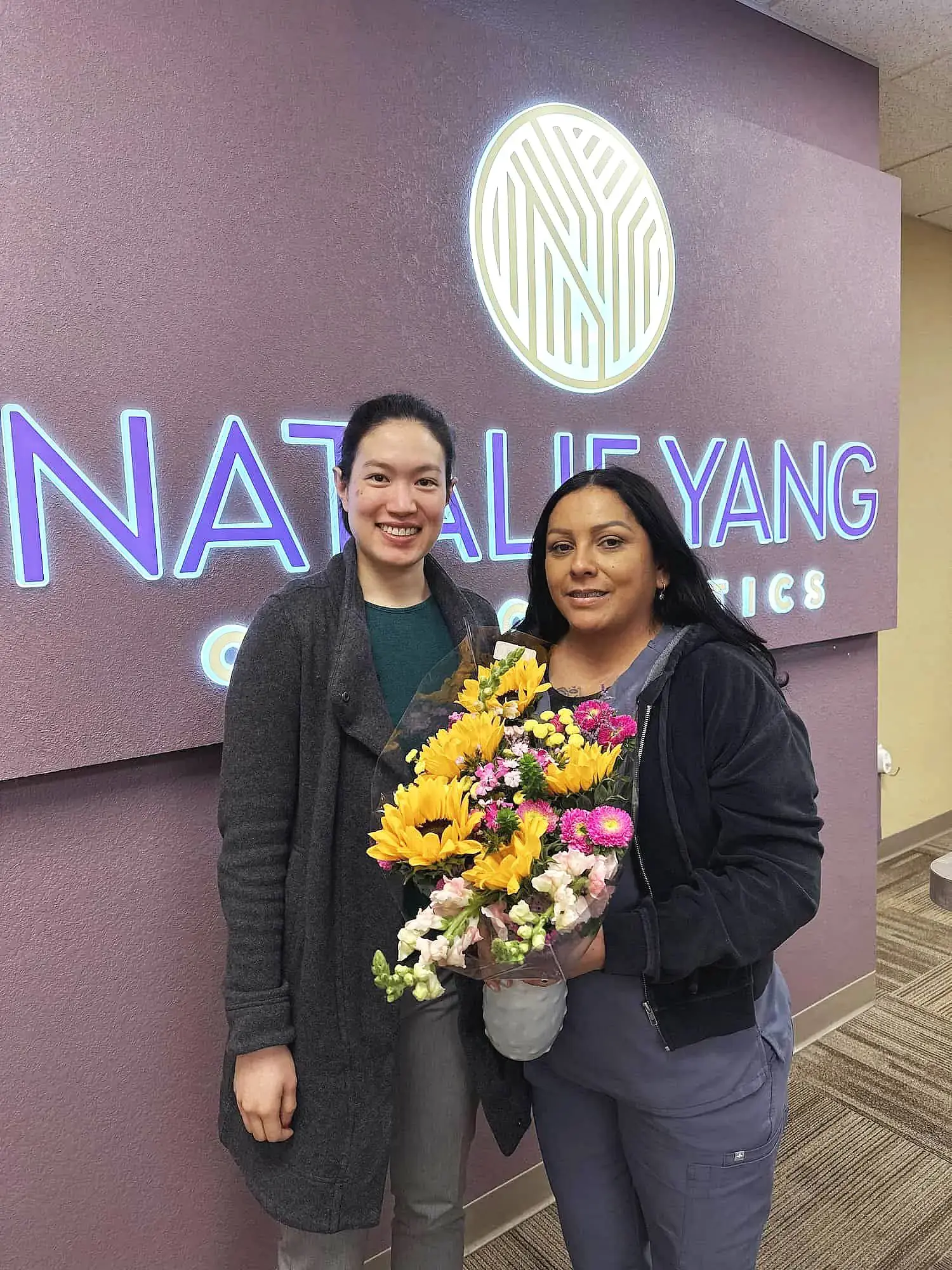 Celebrating tongue thrust progress, two women with flowers stand in front of Natalie Yang Orthodontics in Vacaville, CA. Celebrating tongue thrust progress, two women with flowers stand in front of Natalie Yang Orthodontics in Vacaville, CA.