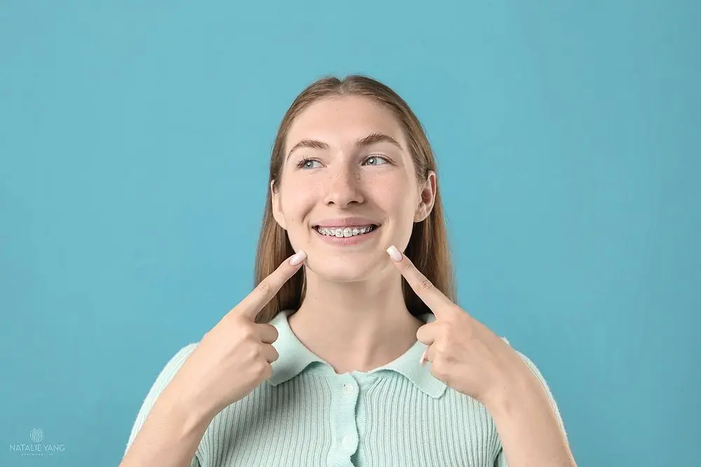 girl pointing her metal braces light blue background - How to Get Braces Glue Off Teeth in Vacaville, CA