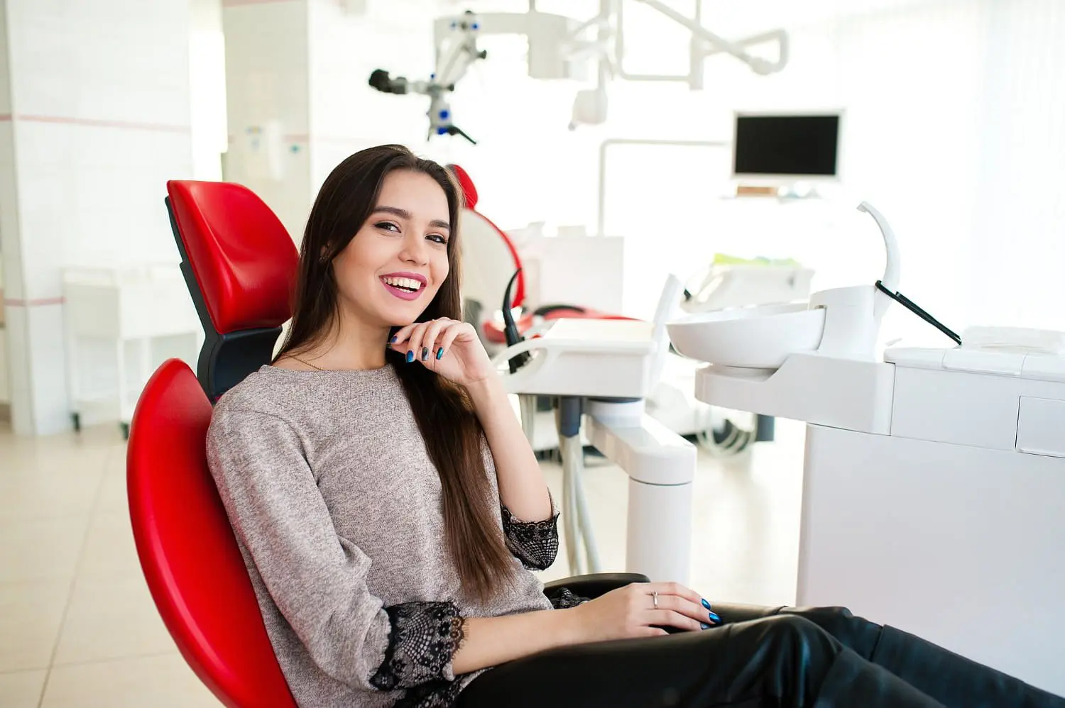 A young woman with long hair smiles in a red dental chair after dental care from best Orthodontist at Natalie Yang Orthodontics Orthodontics in Vacaville, CA.