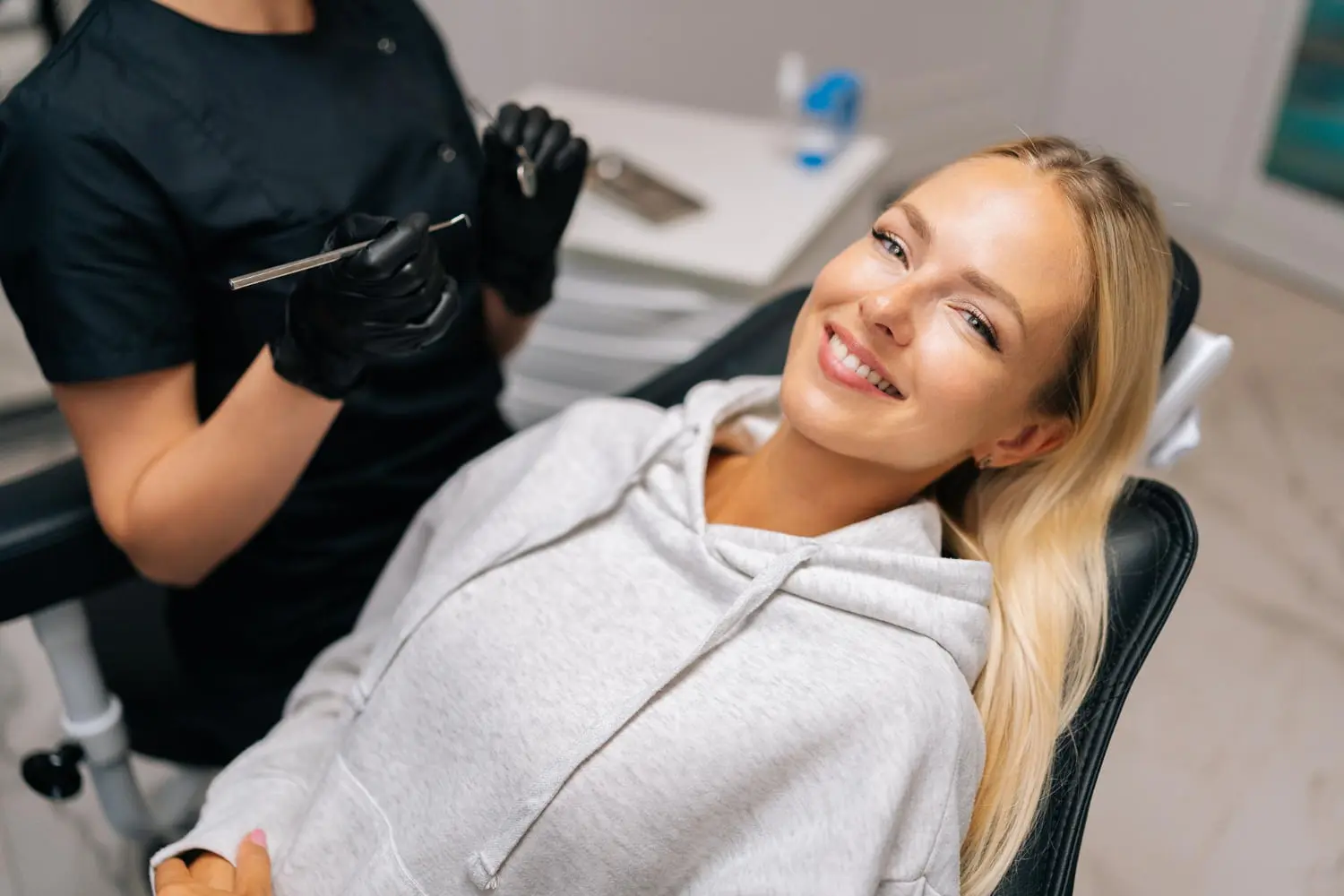 At Natalie Yang Orthodontics in Vacaville, CA, a woman in a grey hoodie smiles in a dental chair as a professional prepares for surgical orthodontics.