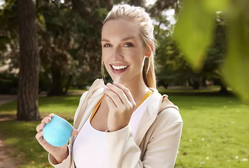 A woman with long hair smiles while holding a clear aligners from Adult Orthodontics at Natalie Yang Orthodontics in Vacaville, CA