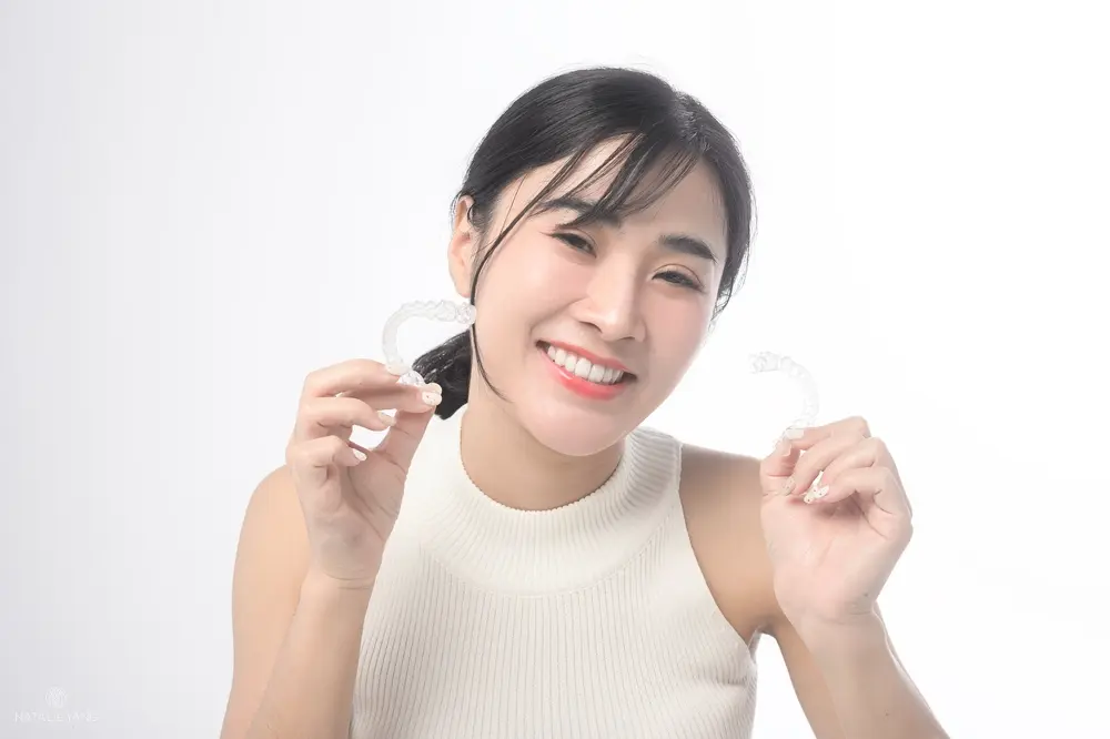 young smiling woman holding invisalign clear aligners white background studio dental - How Long Does Invisalign Take in Vacaville, CA 