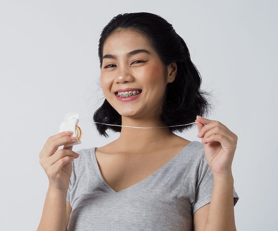 Smiling young woman with metal braces holds dental floss, featured by Natalie Yang Orthodontics in Vacaville, CA.